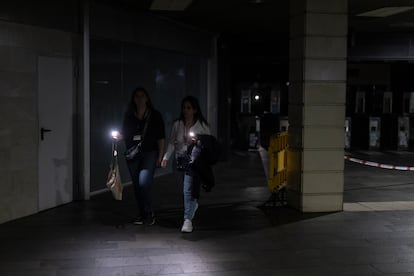 Dos mujeres se iluminan con sus teléfonos móviles tras salir del acceso del metro de Plaza Cataluña en Barcelona, el 28 de abril.