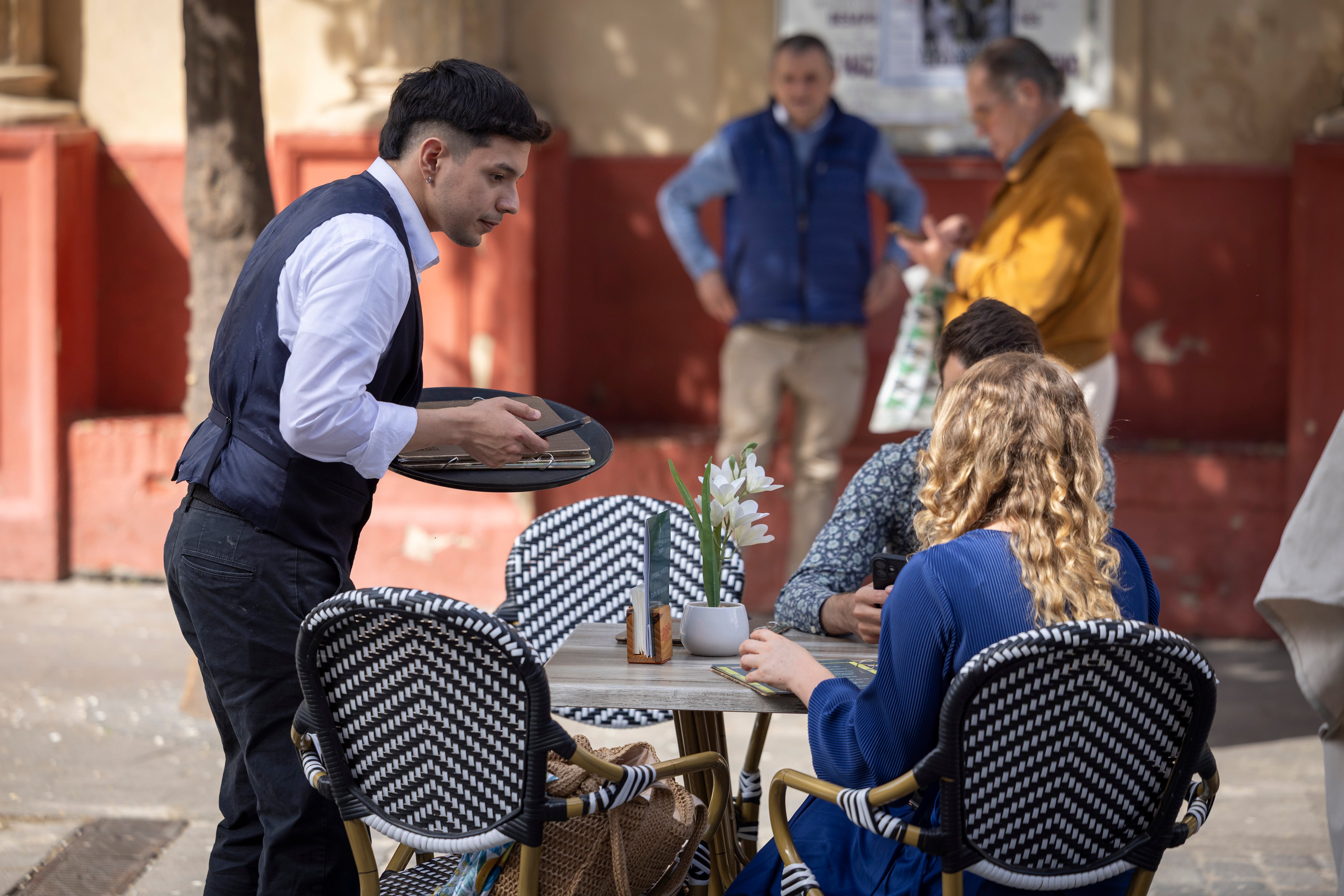 Un camarero atiende a unos clientes en una terraza de Sevilla.